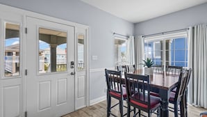 Ein Essbereich mit Holztisch und -stühlen, einem Blumentopf und Blick auf benachbarte Häuser durch die Fenster.
