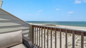 A beach view from a balcony with a wooden railing, a sandy beach, and the ocean.