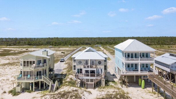 A beachfront property with three houses connected by a pathway, featuring balconies and a sandy beach.