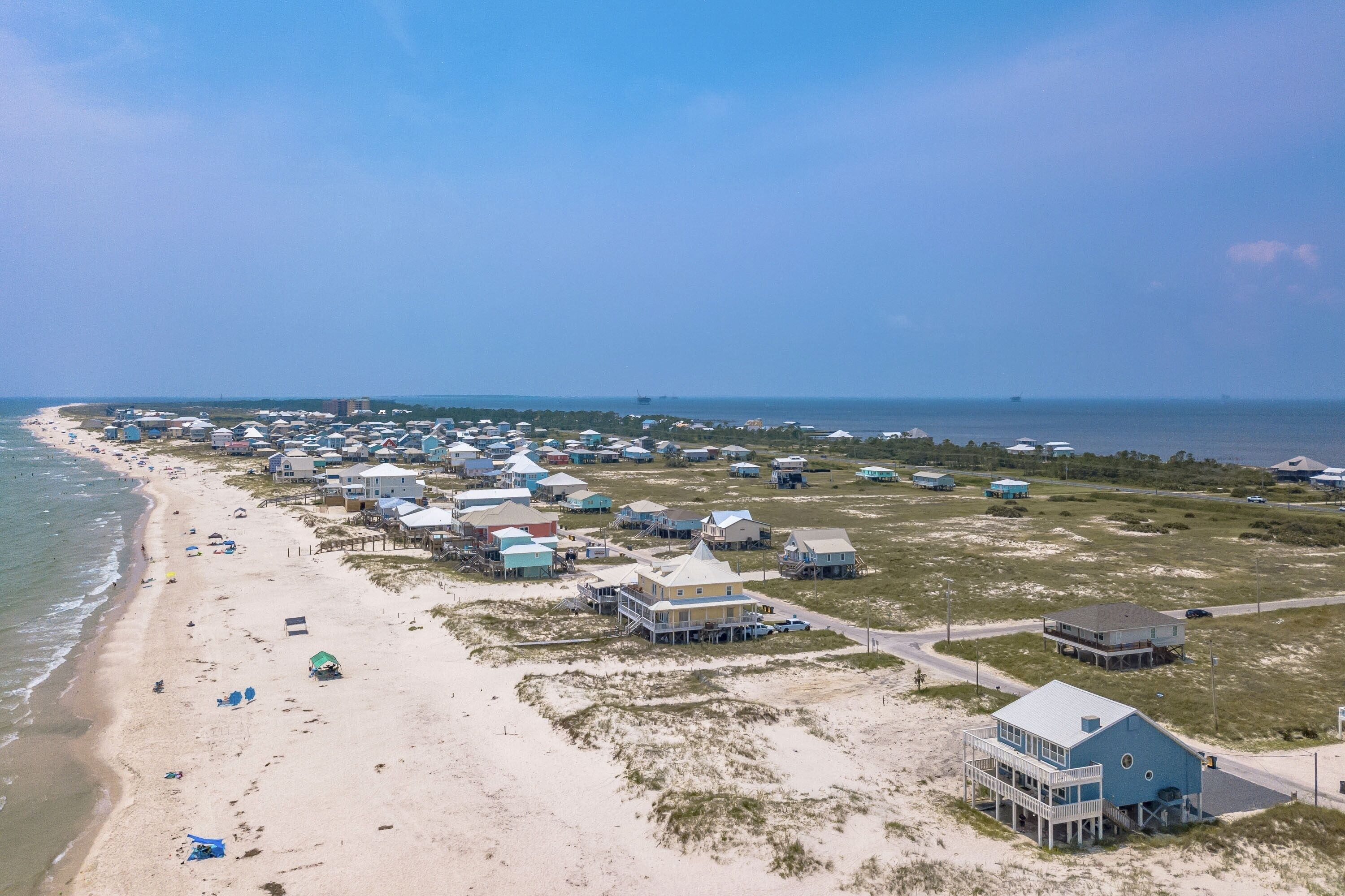 Vista aérea de una zona costera con casas frente al mar, una playa arenosa y el océano.