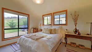 A bedroom with a large bed, two bedside tables, a dresser, and a window with a view of the outside. - Moon River Retreat - Panoramic water views (Gardners Bay)