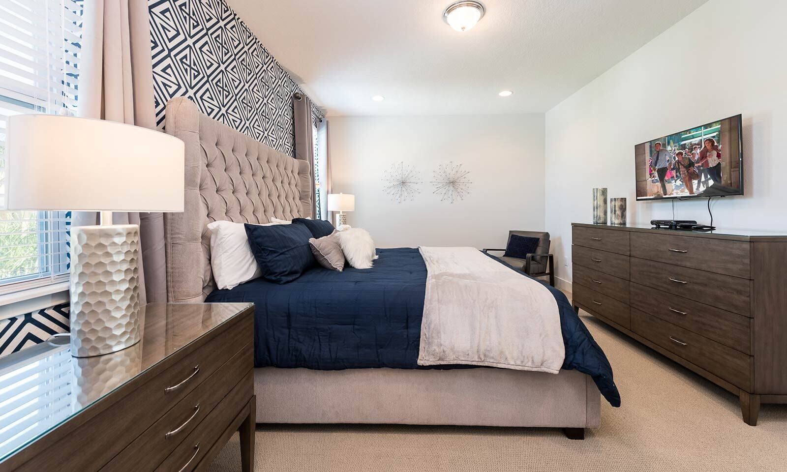 A modern bedroom with a large bed, a nightstand, a dresser, and a TV on the wall.