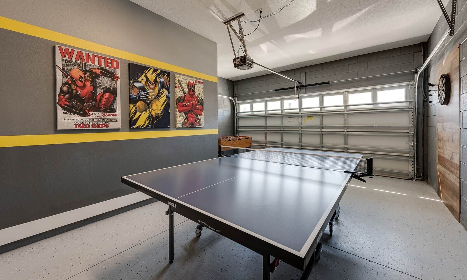 A ping pong table in a garage with a garage door, a projector, and three posters on the wall.