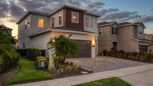 A modern two-story house with a garage, surrounded by well-maintained landscaping and a paved driveway. - Modern 4 Bedroom Home with Game Room in Encore Resort (Kissimmee)