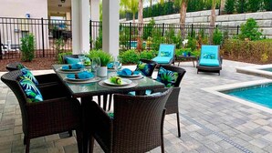 An outdoor patio with a dining table set for two, surrounded by wicker chairs with blue cushions. - Modern 4 Bedroom Home with Game Room in Encore Resort (Kissimmee)