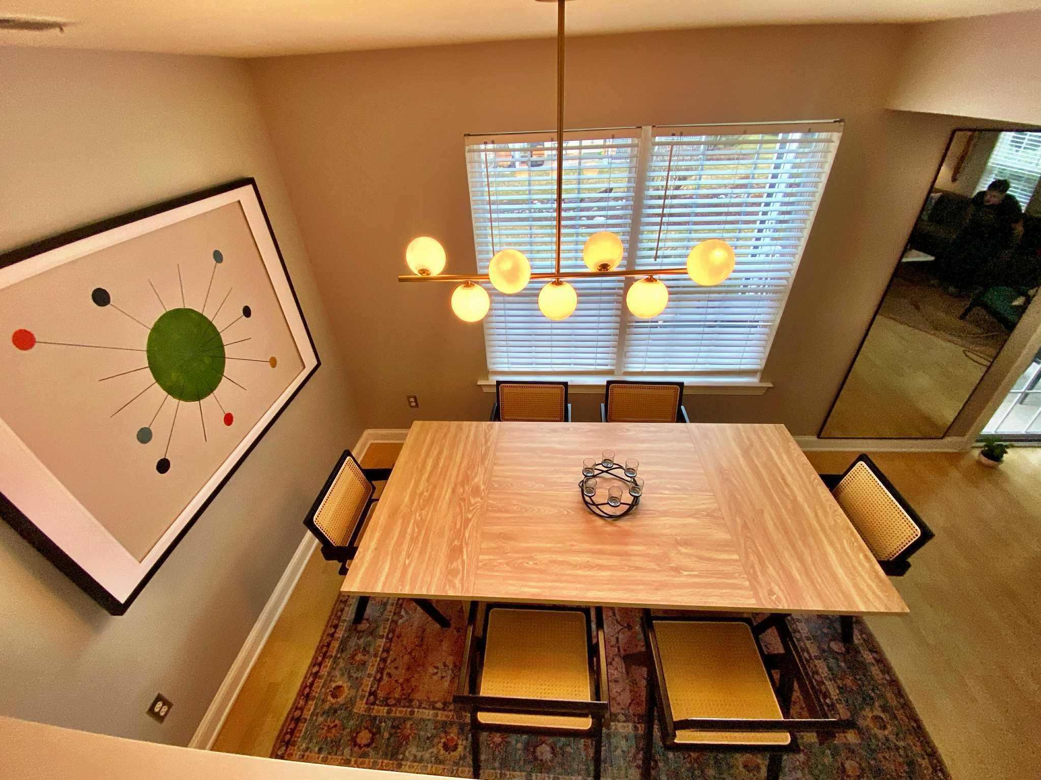 A dining area with a wooden table, chairs, a chandelier, and a large abstract painting on the wall.