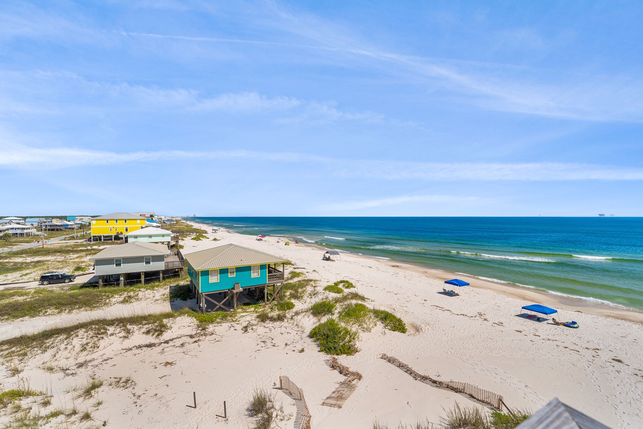 A beach house with a porch, a sandy beach, and the ocean.