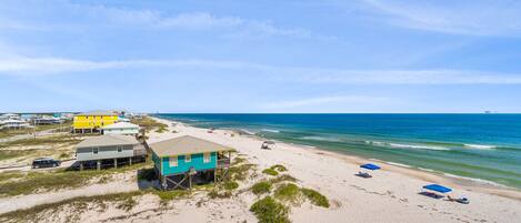 A beach house with a porch, a sandy beach, and the ocean.