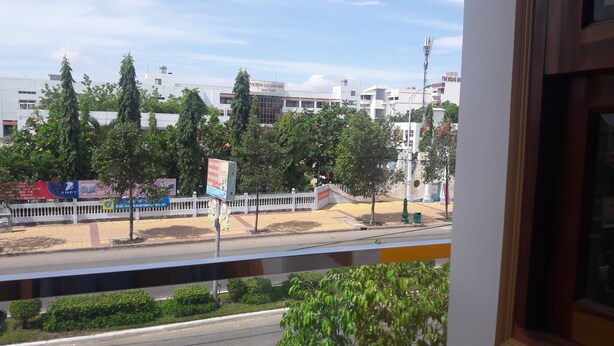 A view from a balcony overlooking a street with buildings, trees, and a white fence.