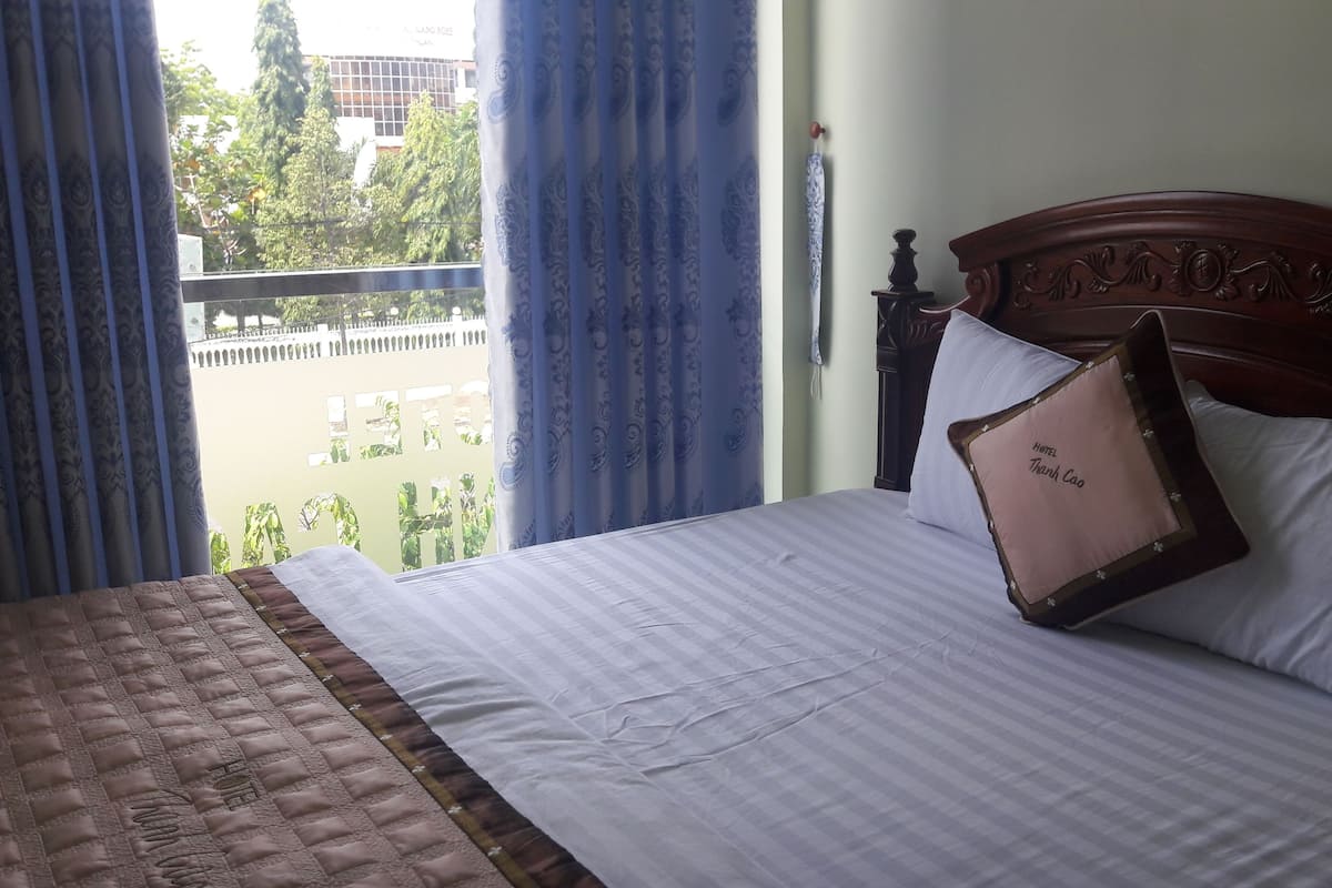 A hotel room with a bed, a view of the outside, and a window with curtains.
