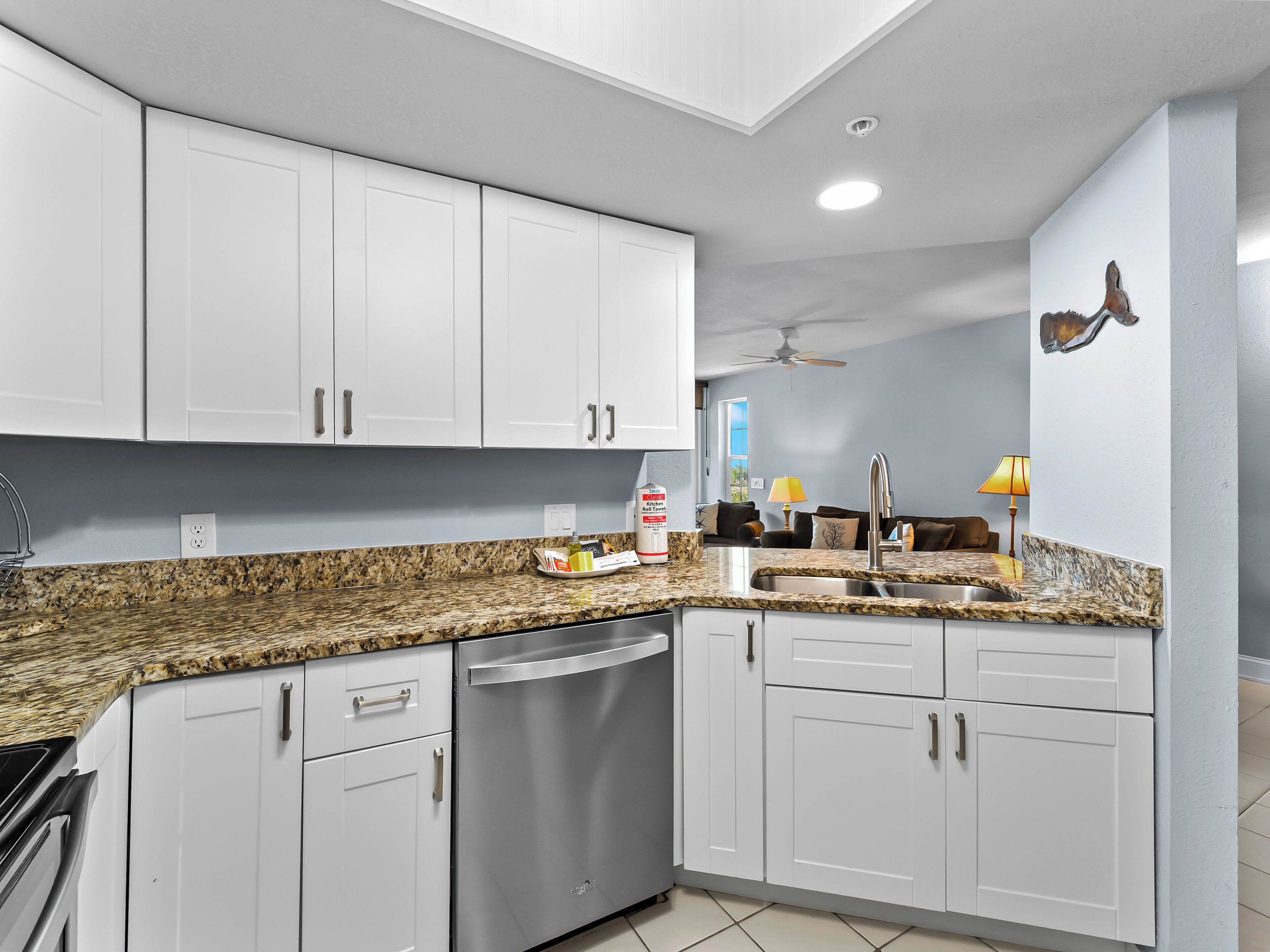 A modern kitchen with white cabinets, granite countertops, stainless steel appliances, and a ceiling fan.