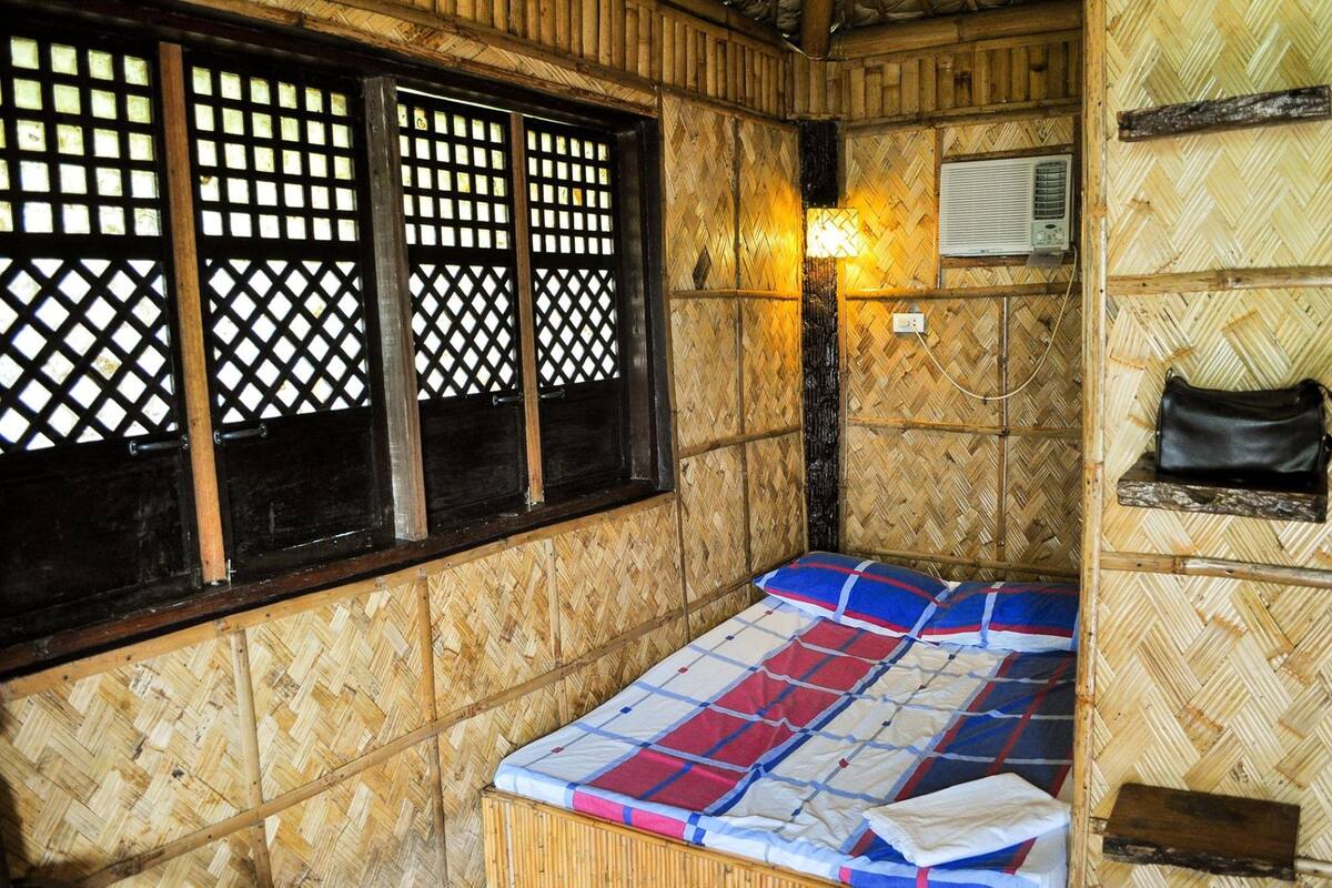 A room with a bed, a window with a lattice design, a wall-mounted air conditioning unit, and a wall-mounted lamp.