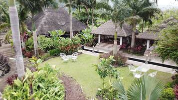 A tropical garden with thatched-roof structures, a grassy lawn, and various tropical plants.