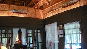 A room with a thatched roof, wooden furniture, and a bed with a blue bedspread. - Tierra de Lago (Los Banos)
