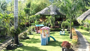 A lush garden with a play area, a thatched-roof structure, and a pathway. - Tierra de Lago (Los Banos)