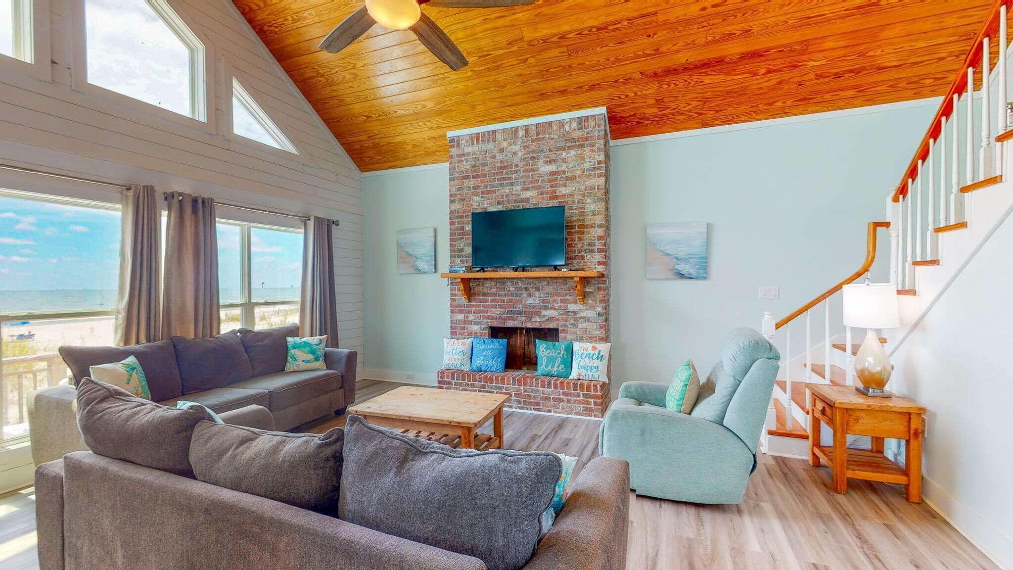 A spacious living room with a fireplace, a sofa, a chair, and a TV mounted on a brick wall.