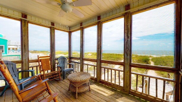 Una terraza de madera con muebles de mimbre y vistas a la playa.