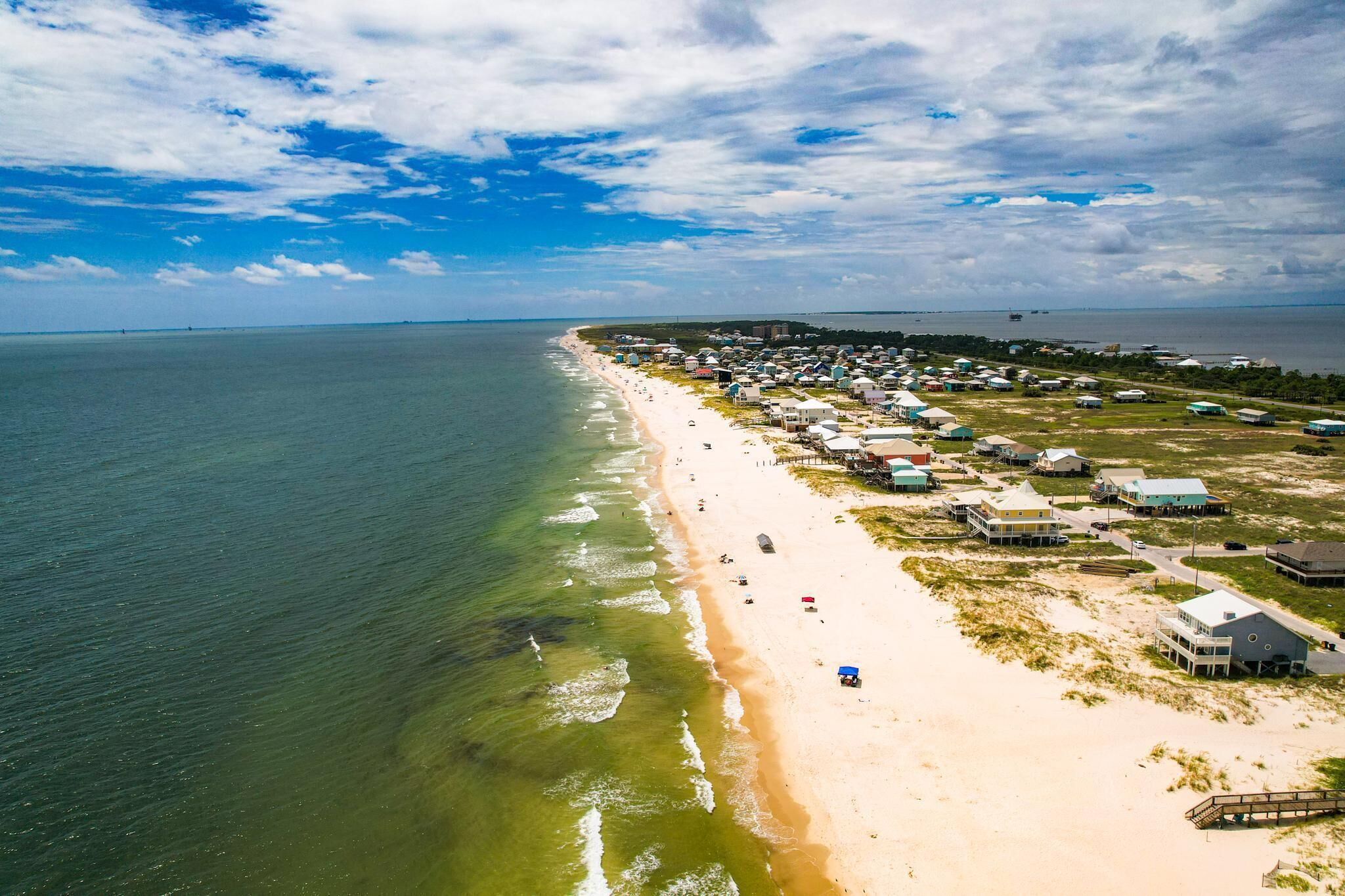 An aerial view of a beachside resort with multiple buildings, a sandy beach, and a clear view of the ocean.