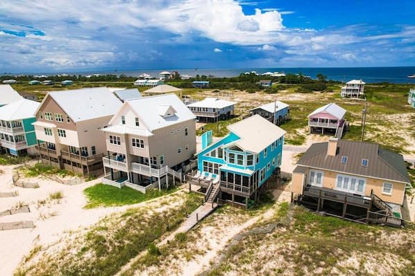 A coastal residential area with multiple houses, some with elevated structures, and a beach in the background.
