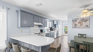 A modern kitchen with grey cabinets, a white island, and a dining area with a table and chairs. - Affordable Renovated 3 Bd/2 Ba home steps from the beach with pool/tennis access (Gulf Shores)