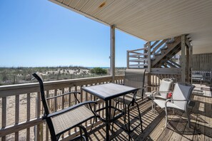Eine Holzterrasse mit Tisch und Stühlen, einem Geländer und Blick auf den Strand.