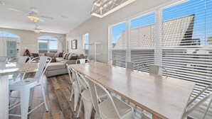 Une cuisine spacieuse avec une table et des chaises en bois, un four encastré et une grande fenêtre équipée de stores.
