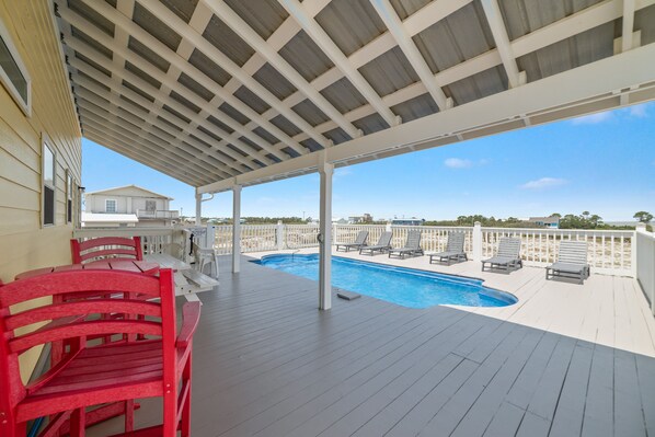 A covered outdoor area with a pool, red chairs, and a view of the beach.