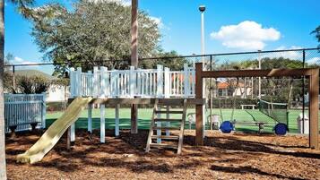 A playground with a slide, climbing structure, and a fenced tennis court area.