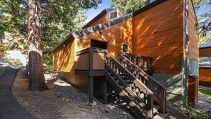 Una cabaña de madera con una escalera que lleva a una terraza, rodeada de árboles.