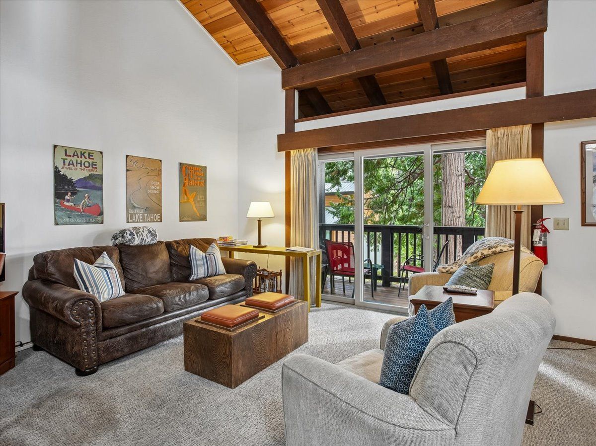 A living room with a brown leather sofa, a grey armchair, and a wooden coffee table. There are posters on the wall and a lamp on a side table.