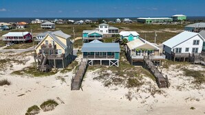 A coastal area with multiple beachfront properties featuring elevated structures, wooden walkways, and a clear view of the ocean.