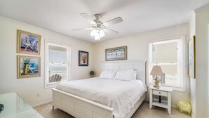 A bedroom with a bed, a ceiling fan, a bedside table, and artwork on the walls.