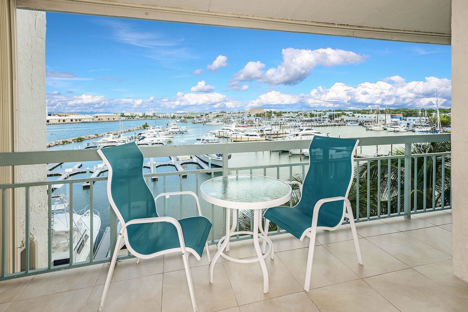 A balcony with two chairs and a table, overlooking a marina with boats and a clear sky.