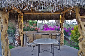 A gazebo with a thatched roof, a stone bench, and a table.