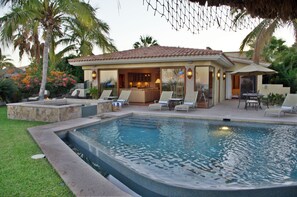 A poolside area with a covered patio, lounge chairs, and a stone planter.