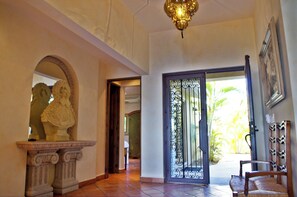 A hallway with a statue, a wrought iron door, and a chair with a rack.