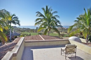 A rooftop terrace with a chair, palm trees, and a view of the ocean.