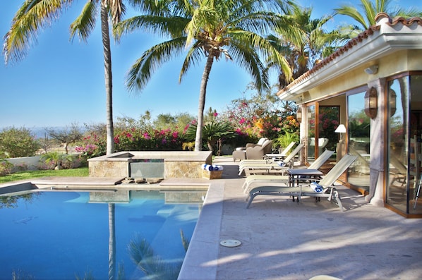 A poolside area with lounge chairs, a palm tree, and a clear view of the sky.