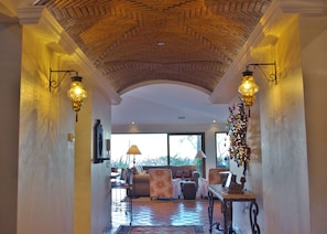 A hallway with a high arched ceiling, two wall-mounted lamps, a sofa, chairs, and a dining table.