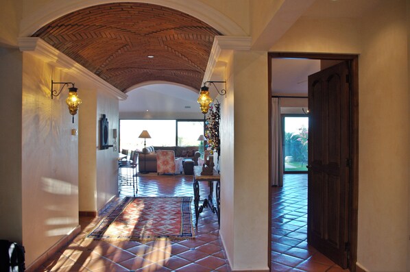 A hallway with a tiled floor, a brick ceiling, and a door leading to a room with a large window.