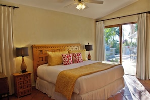 A bedroom with a large bed, two bedside lamps, a wooden nightstand, and a view of the outdoor patio.