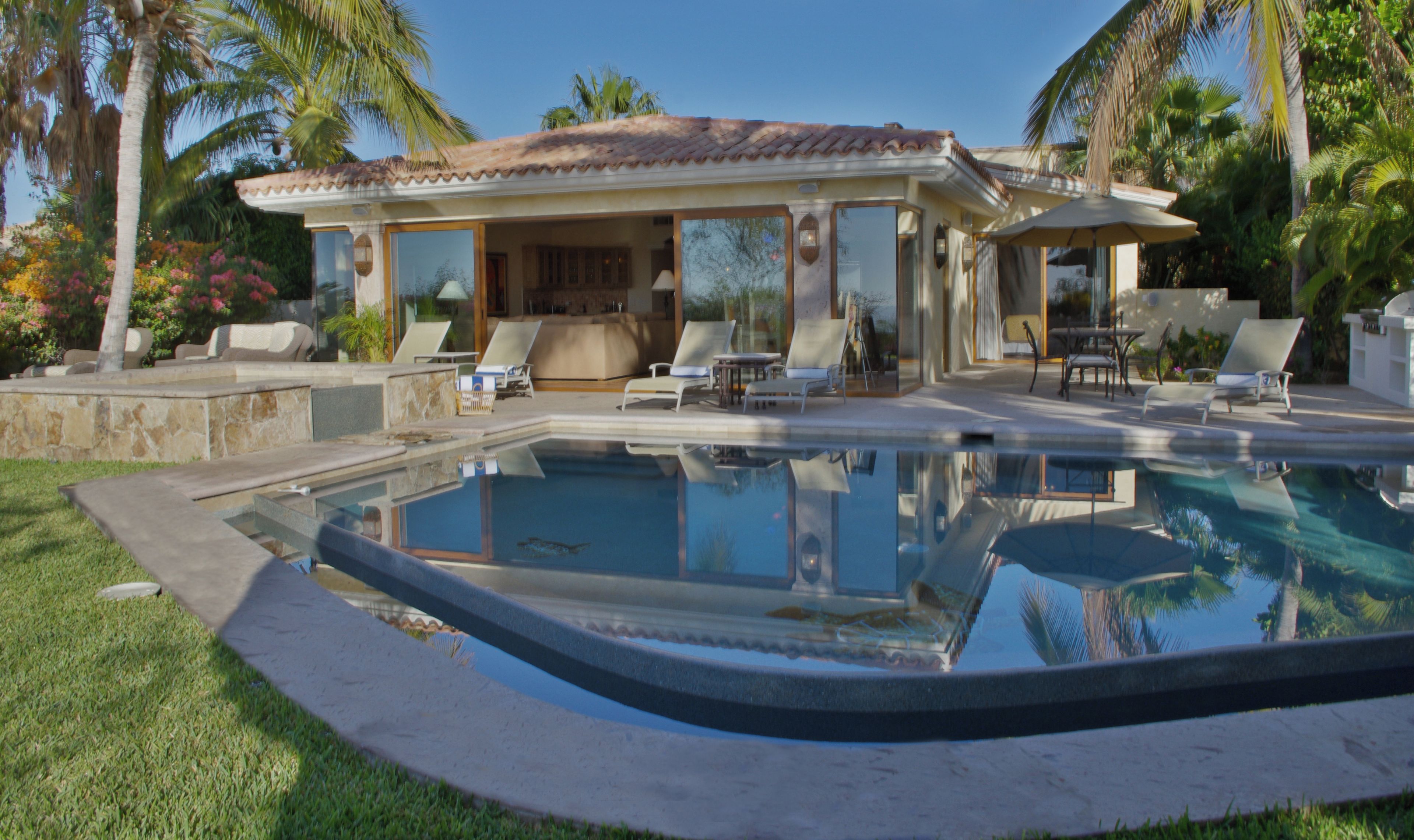 Una casa de piscina moderna con techo de tejas, piscina y asientos exteriores.