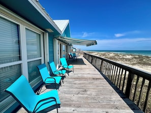 A wooden deck with chairs and a table, overlooking a beach.