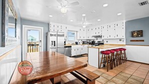 A kitchen with white cabinets, a wooden table, and a bar area with stools. - Mitts-issippi - Charming 4br/2ba Gulf Front Home, Sleeps 10 (Gulf Shores)