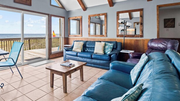 A spacious living room with a large blue leather sofa, a wooden coffee table, and a view of the ocean through a sliding glass door. - Mitts-issippi - Charming 4br/2ba Gulf Front Home, Sleeps 10 (Gulf Shores)