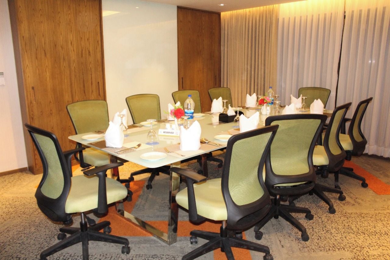 A conference room with a long table, multiple chairs, and a projector screen.
