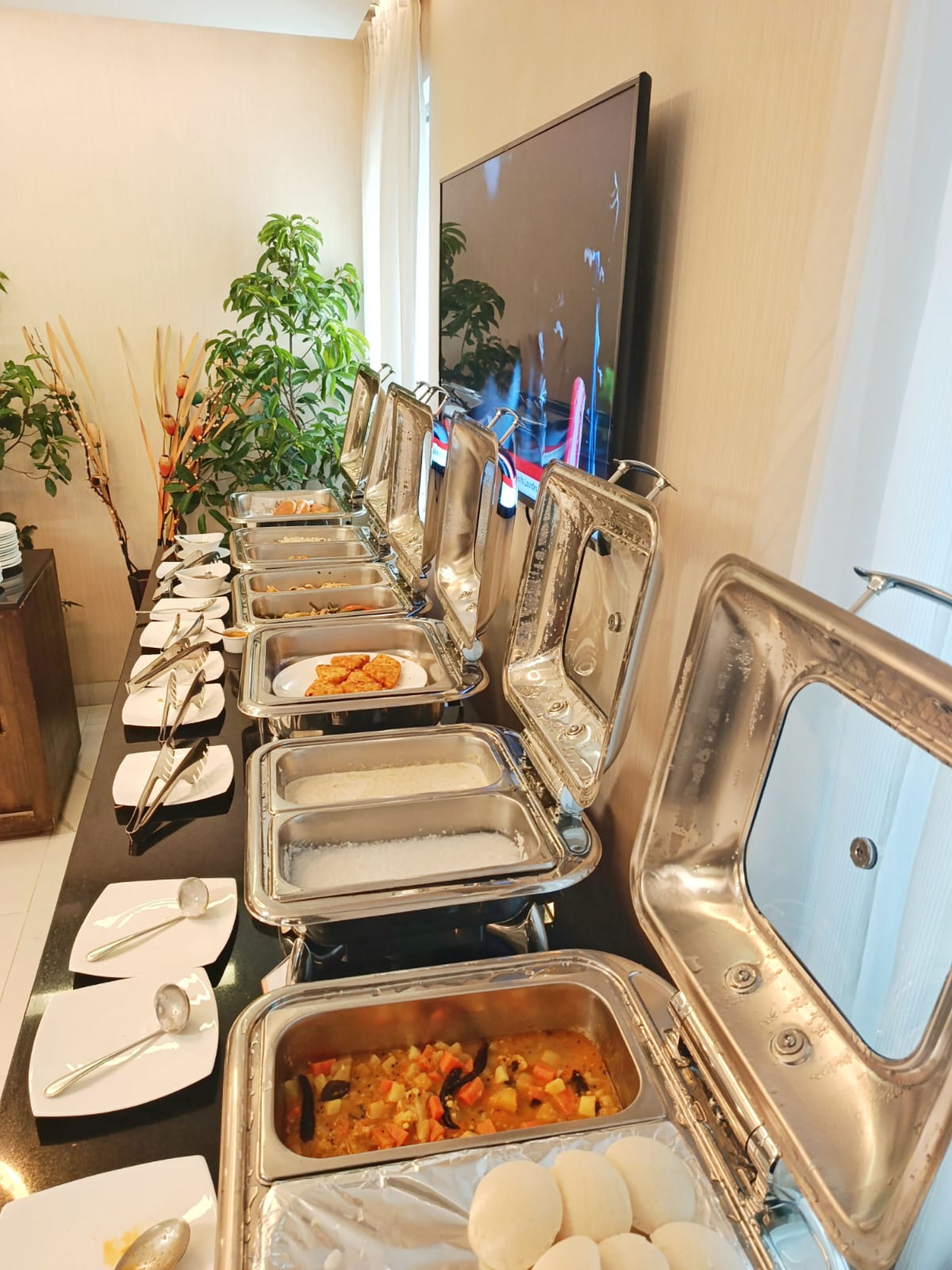 A buffet setup with multiple serving stations, utensils, and a television in the background.