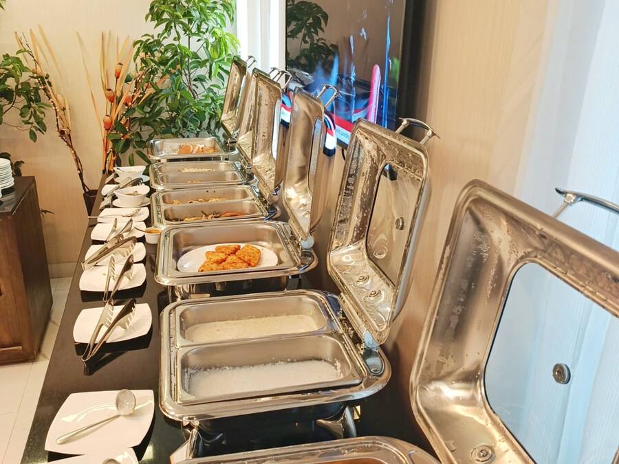 A buffet setup with multiple serving stations, utensils, and a television in the background.