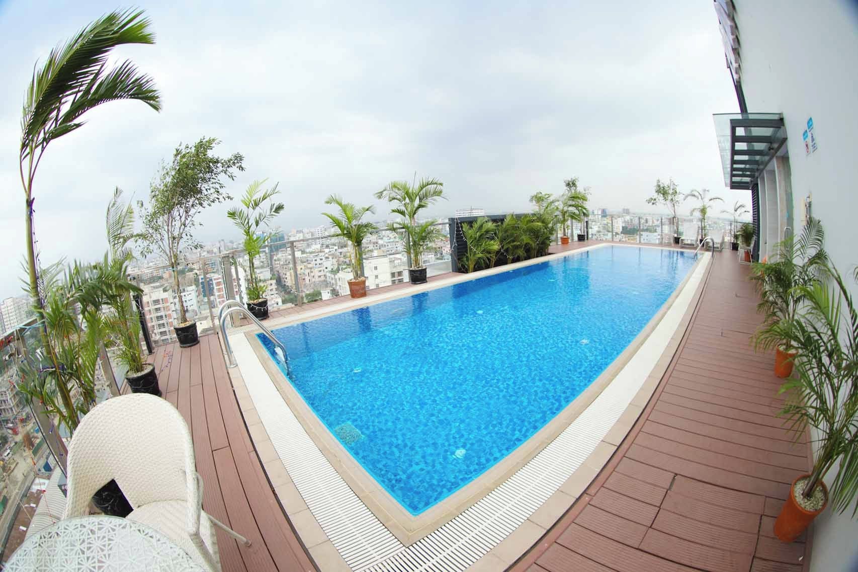 Una piscina en la azotea con vista a la ciudad, rodeada de plantas en macetas y una terraza de madera.