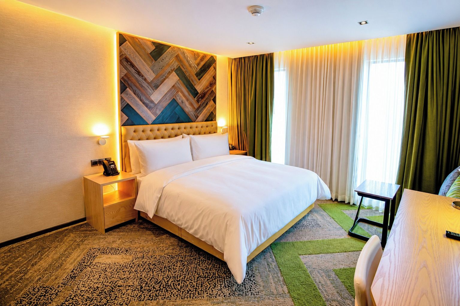 Una habitación de hotel con cama, mesitas de noche, teléfono, lámpara, una pequeña mesa y una silla.